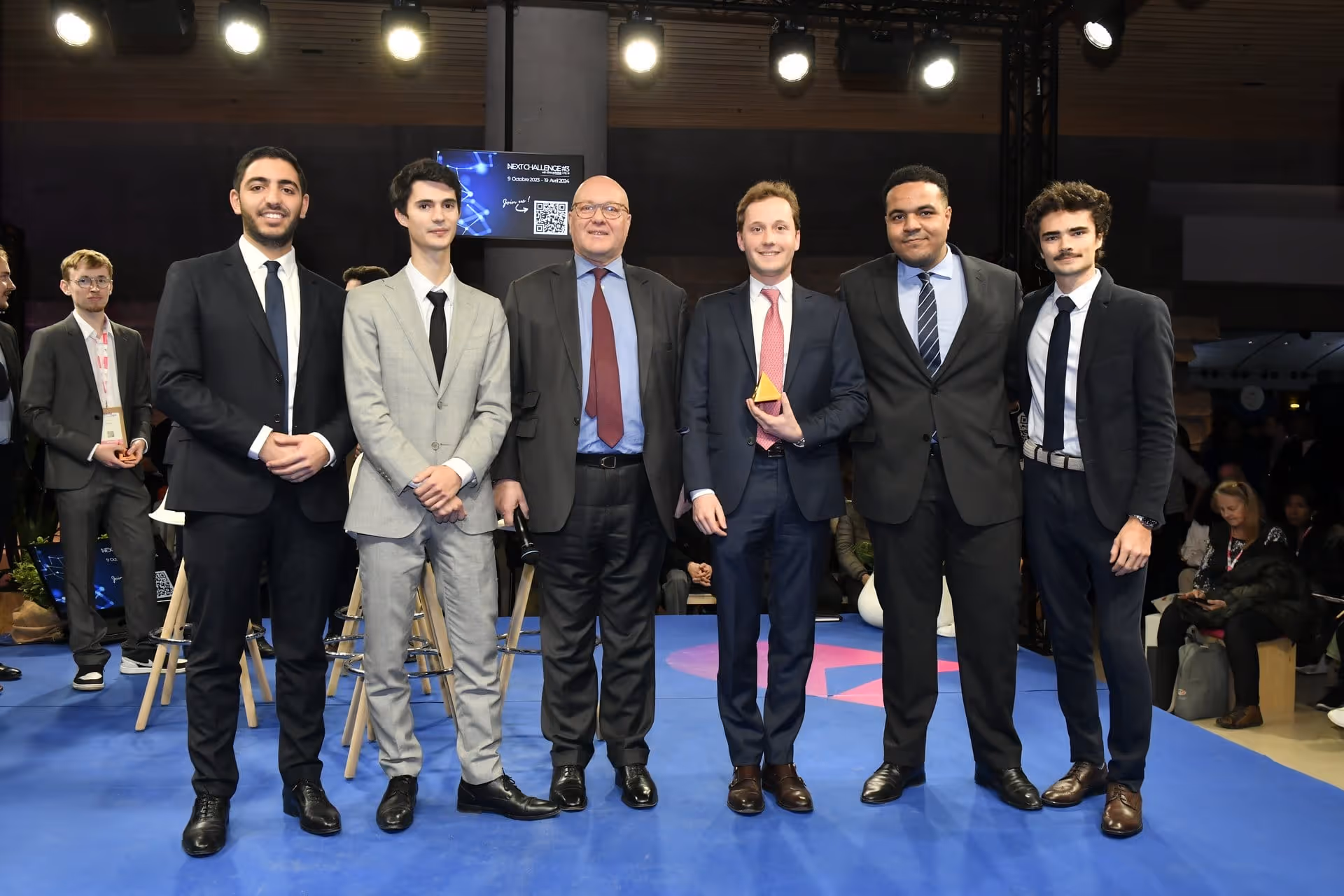 Six hommes en costumes formels posant ensemble sur scène avec un trophée jaune.