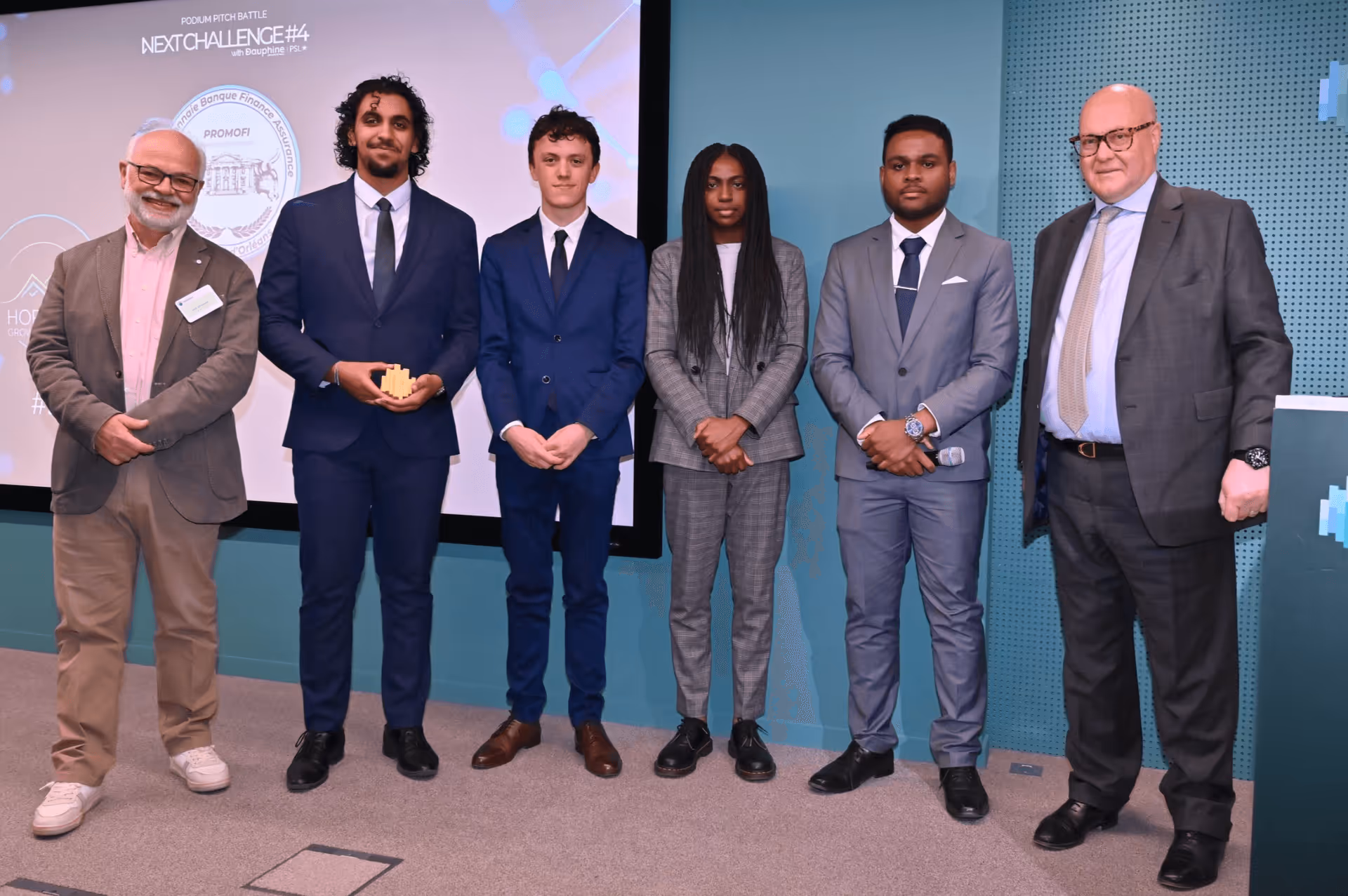Six personnes posant lors d'un concours de pitch, quatre en costume et deux plus âgées en tenue professionnelle.