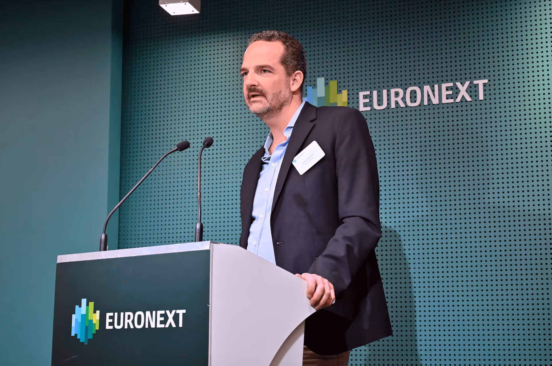 Un homme en costume donne un discours derrière un pupitre avec le logo Euronext.