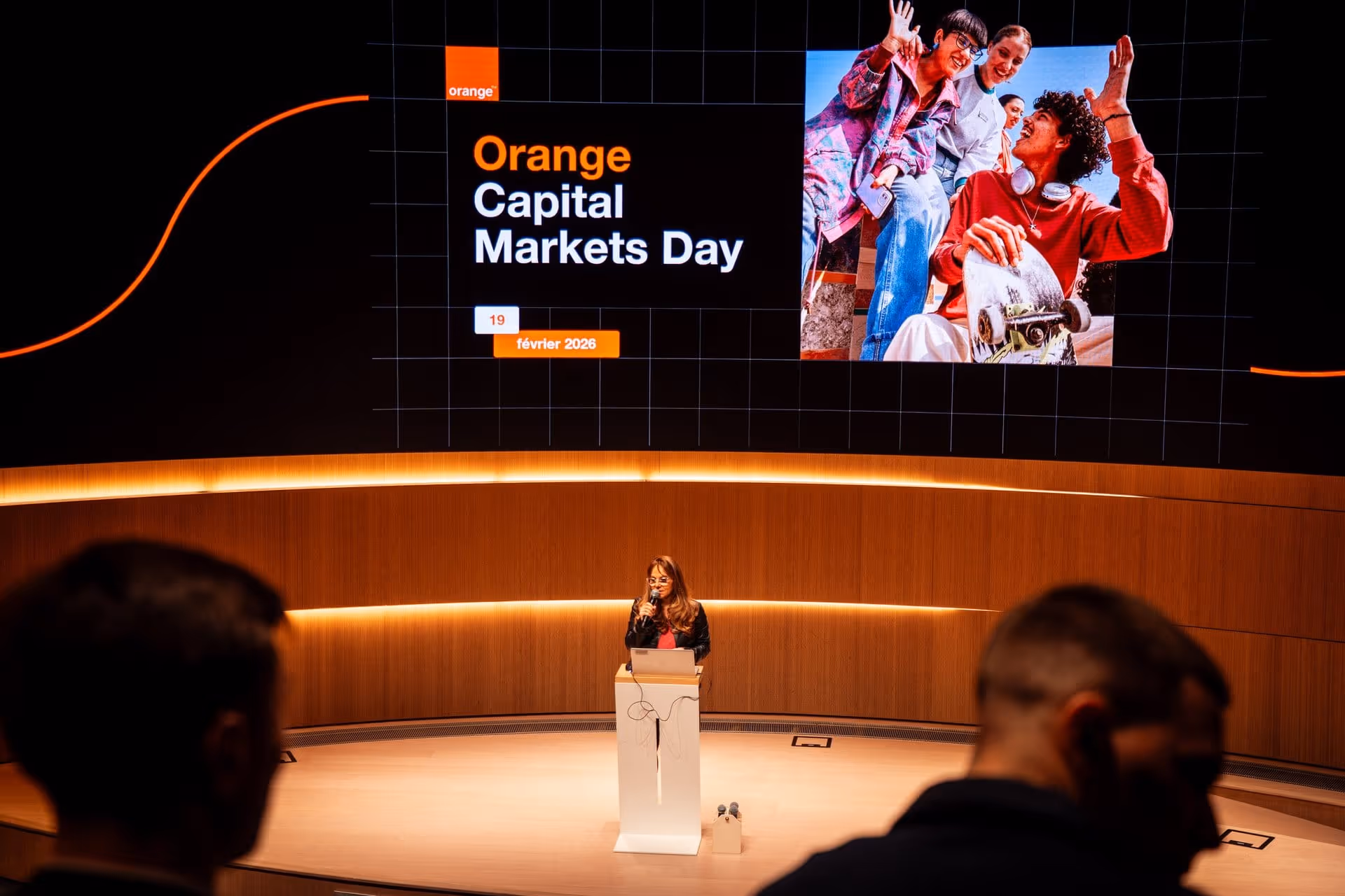 Une femme parle au micro depuis un podium devant un écran affichant Orange Capital Markets Day.