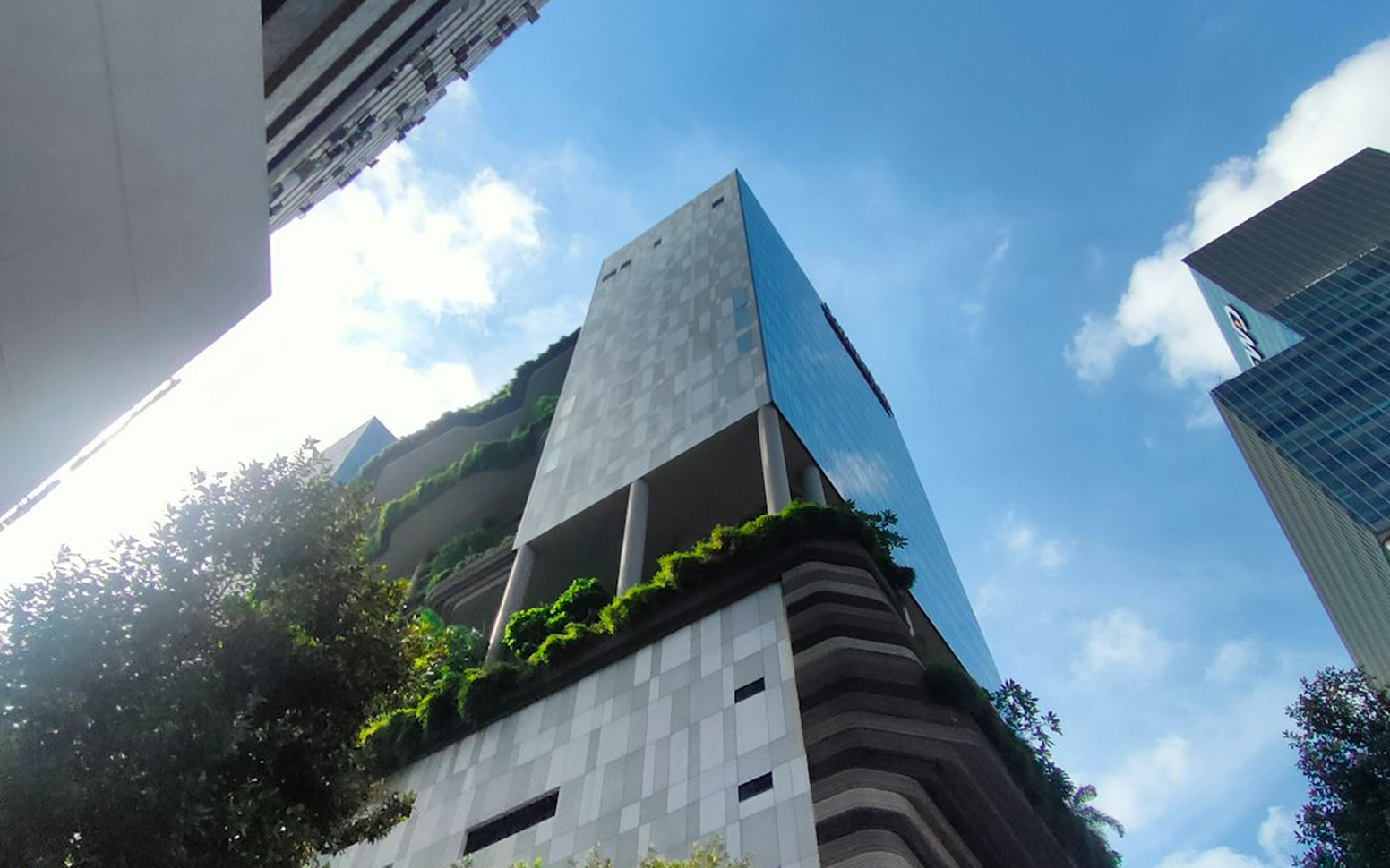 Modern high-rise building with greenery on balconies and terraces under a blue sky with clouds.