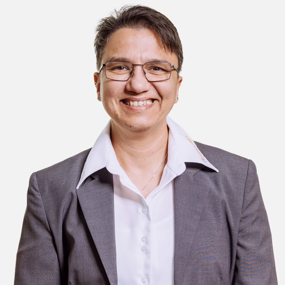 Lächelnde Person mit Brille, weißem Hemd und grauem Blazer vor weißem Hintergrund.
