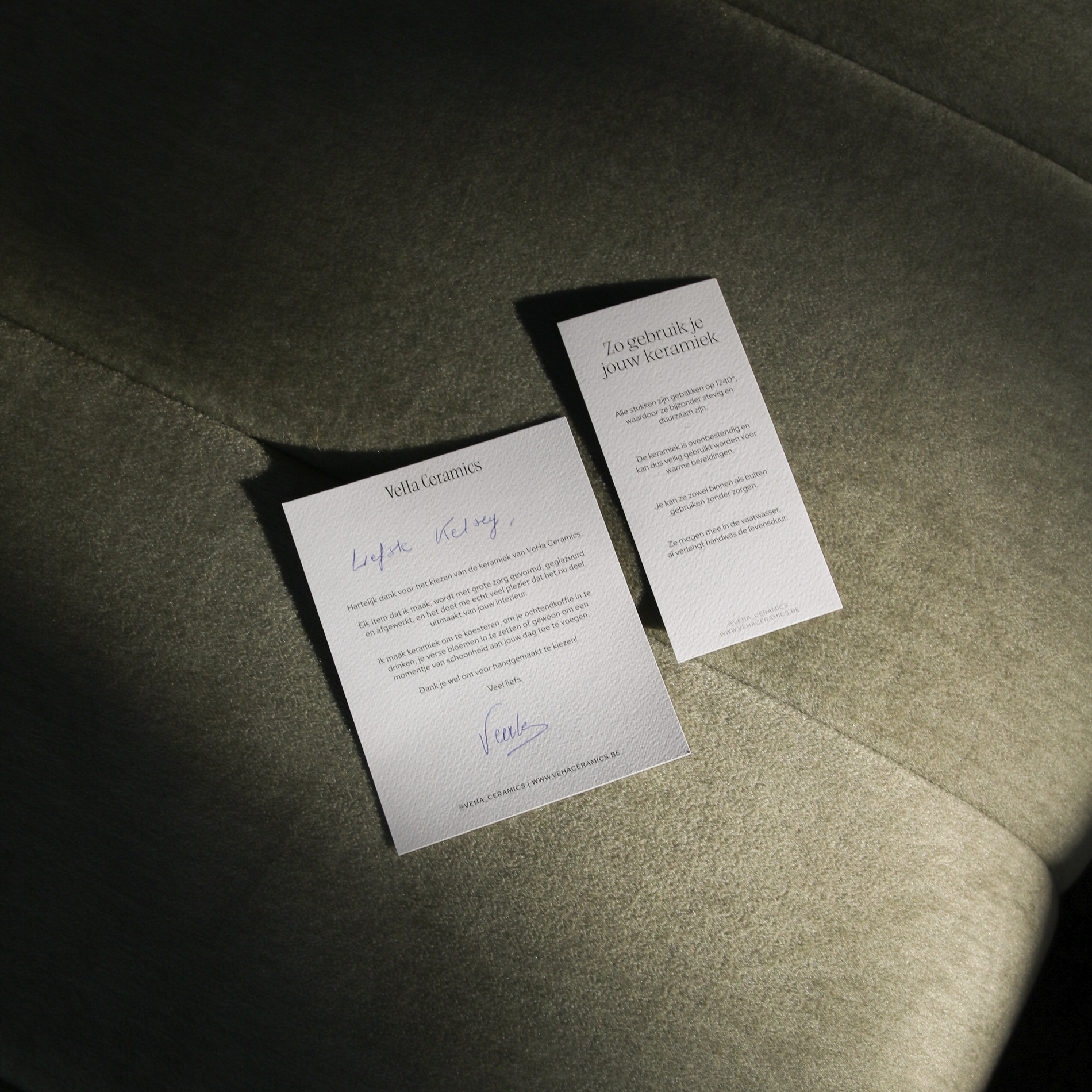 Twee witte kaarten met tekst in het Nederlands liggen op een groene stof, één met een handgeschreven boodschap en de andere met keramiek gebruiksinstructies.