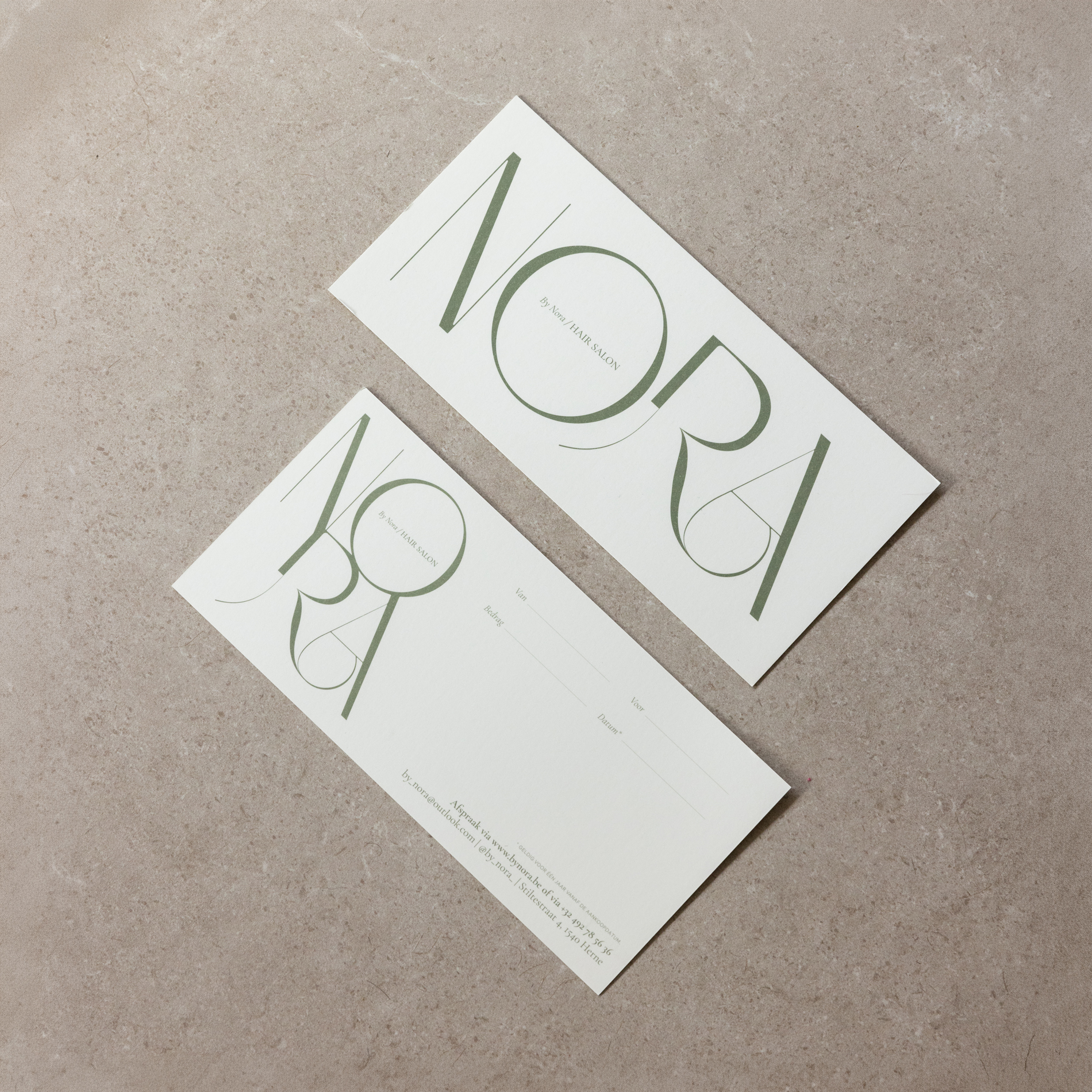 Twee witte cadeaubonnen met het logo NORA in groene sierlijke letters, liggend op een beige marmeren oppervlak.