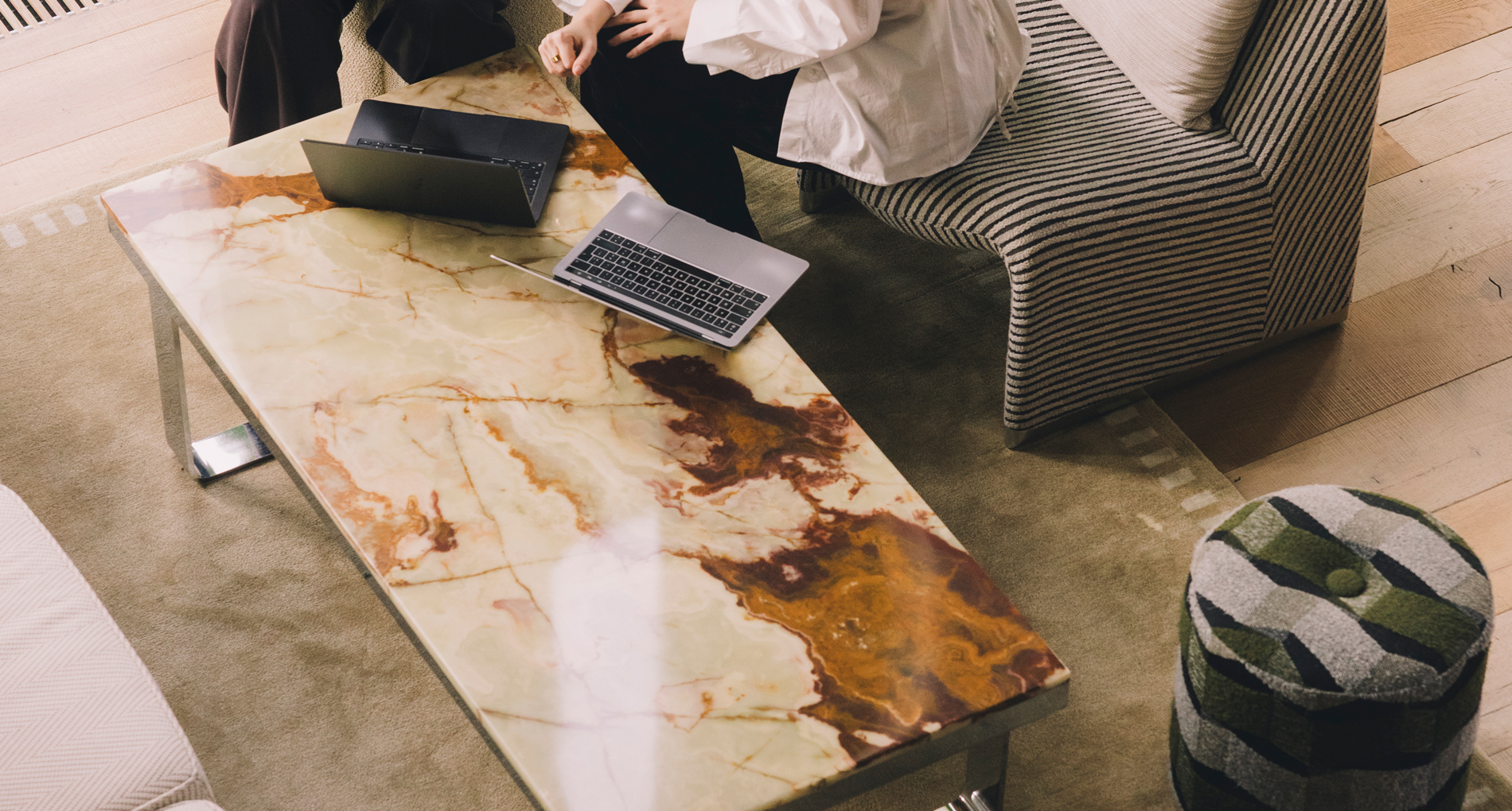 Twee mensen die op een gestreepte bank zitten met twee laptops op een marmeren salontafel in een woonkamer.