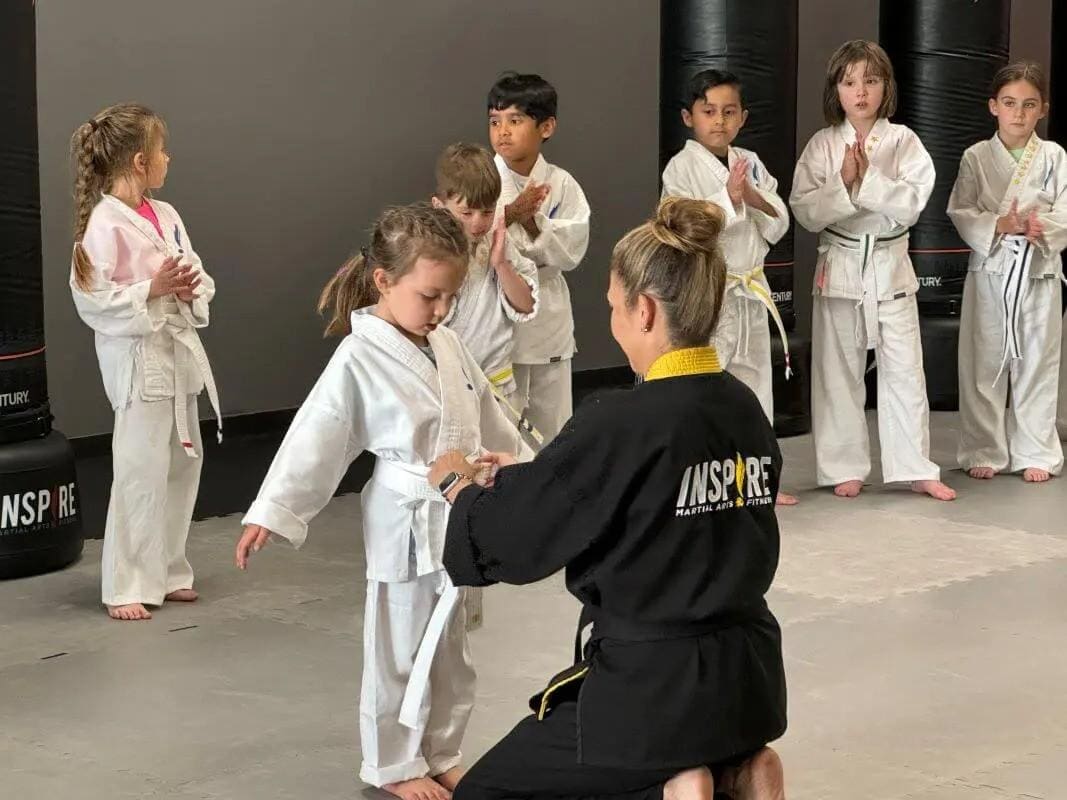 Instructor tying a student’s belt during a beginner self defense class for young children.