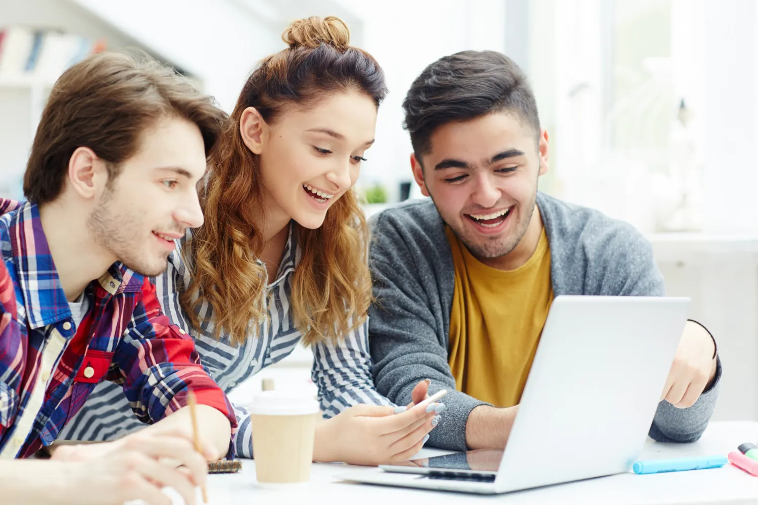 Three young people smiling and looking at a laptop screen together while studying.