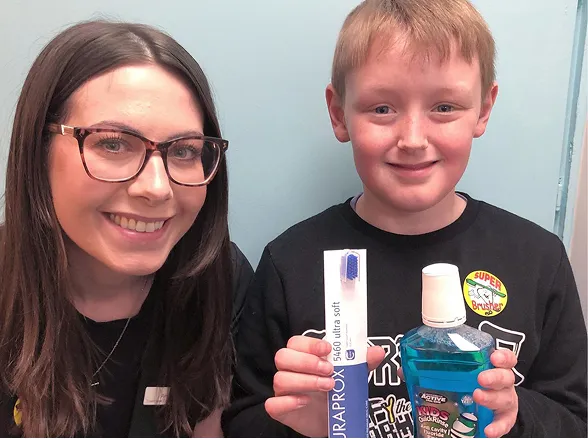 Smiling woman with glasses and a boy holding oral care products including a toothbrush and mouthwash.