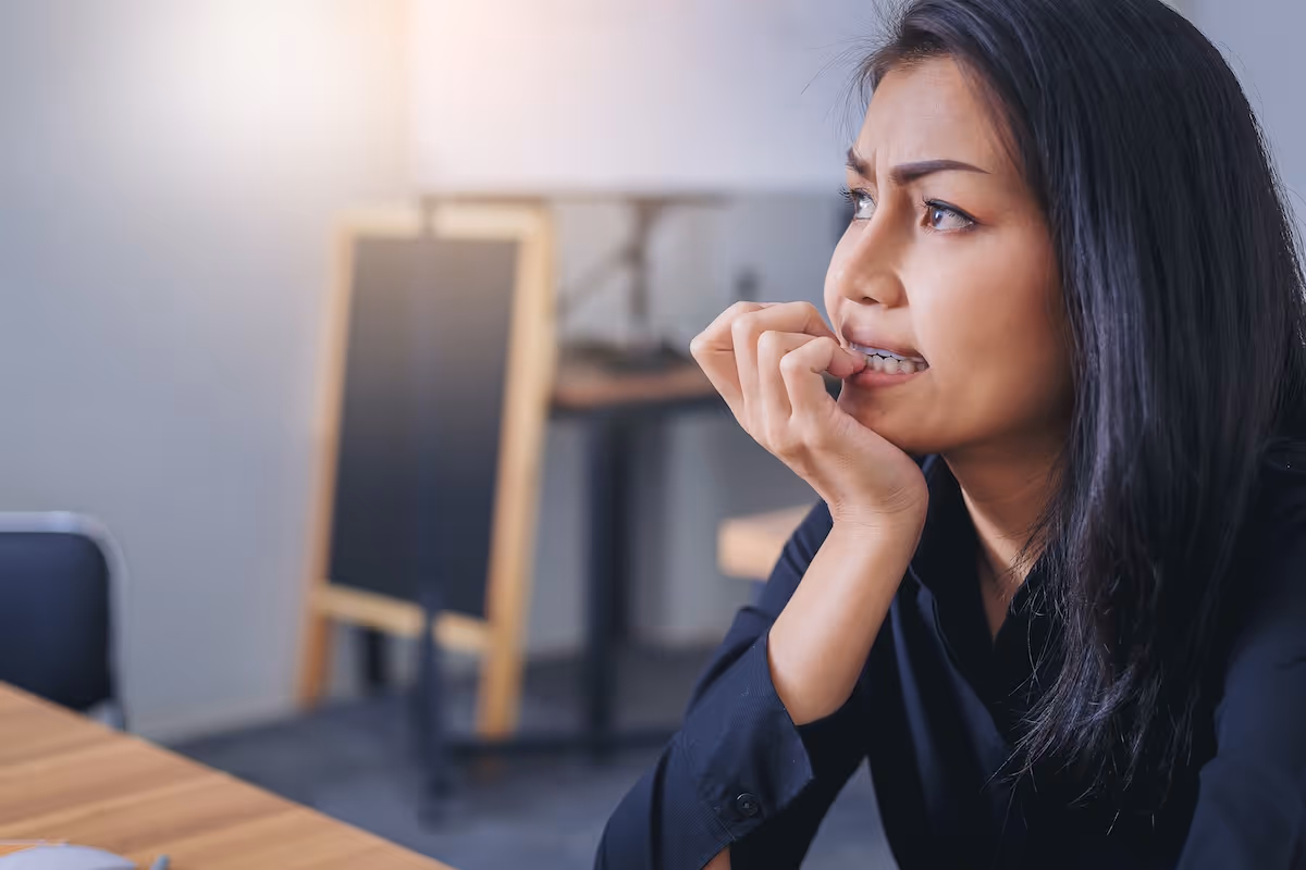 Anxious woman biting her nails sitting at a table in an office setting.