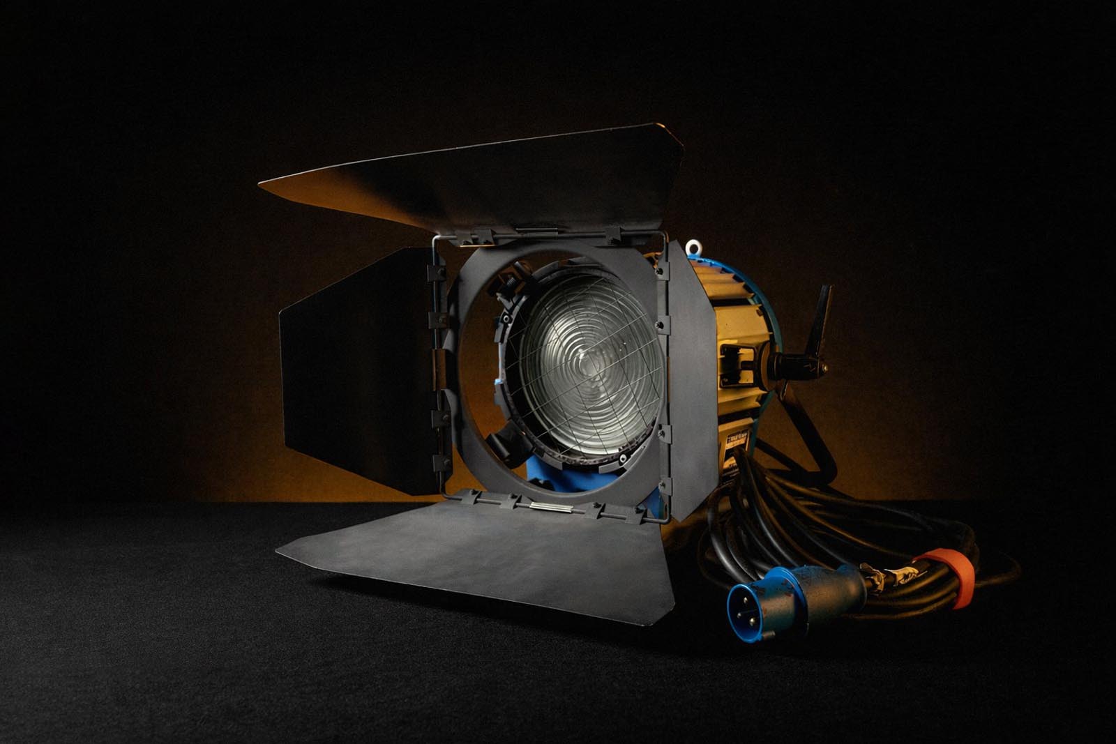 Professional studio spotlight with barn doors and attached cable on a black surface with dark background.