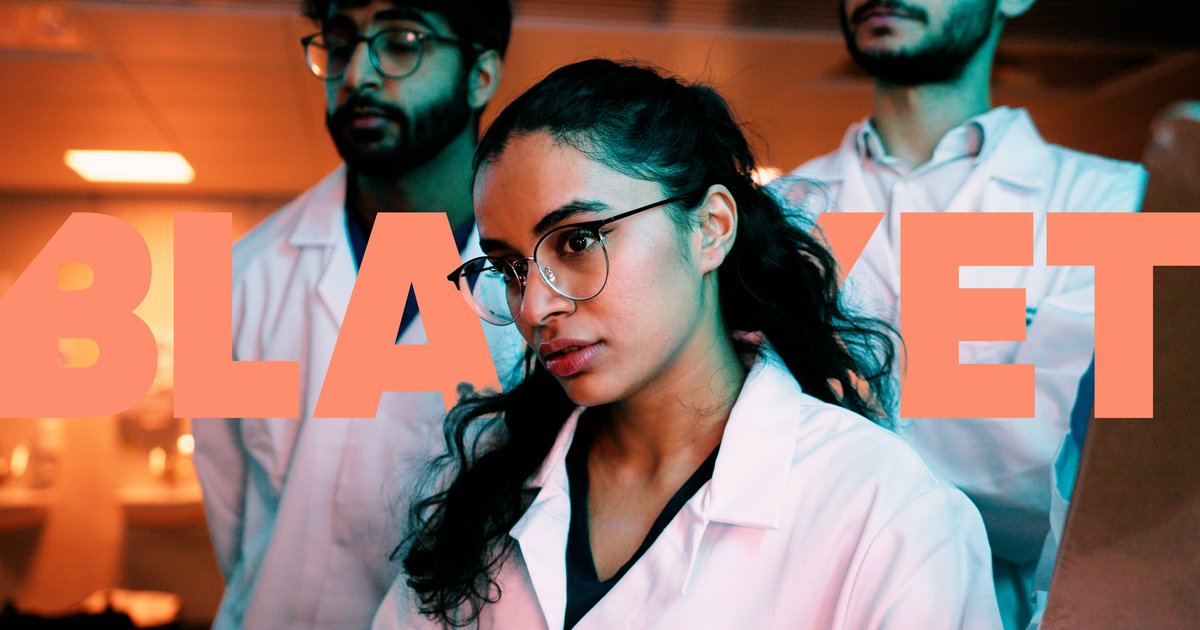 Focused medical professionals in white lab coats in a clinical setting with large orange text partially visible behind them.