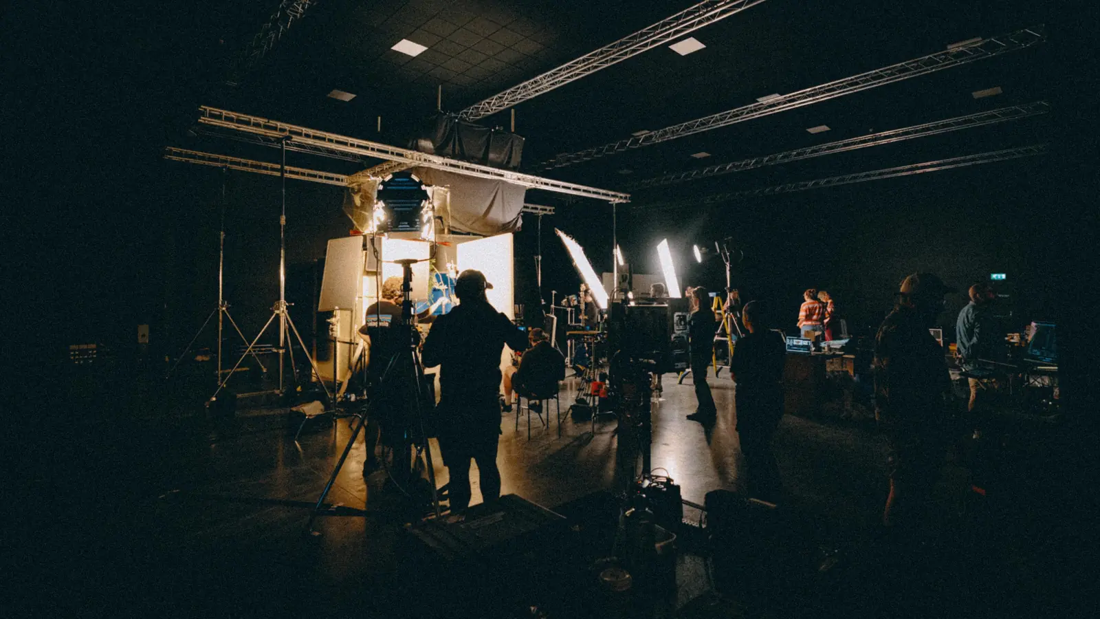 Film crew working on a dimly lit indoor set with bright lights and camera equipment.
