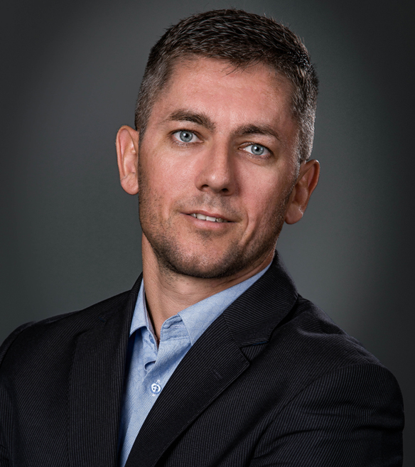 Man in a dark suit and blue shirt against a dark gray background