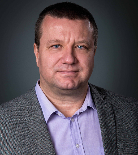 Man in a gray suit and purple shirt against a dark gray background