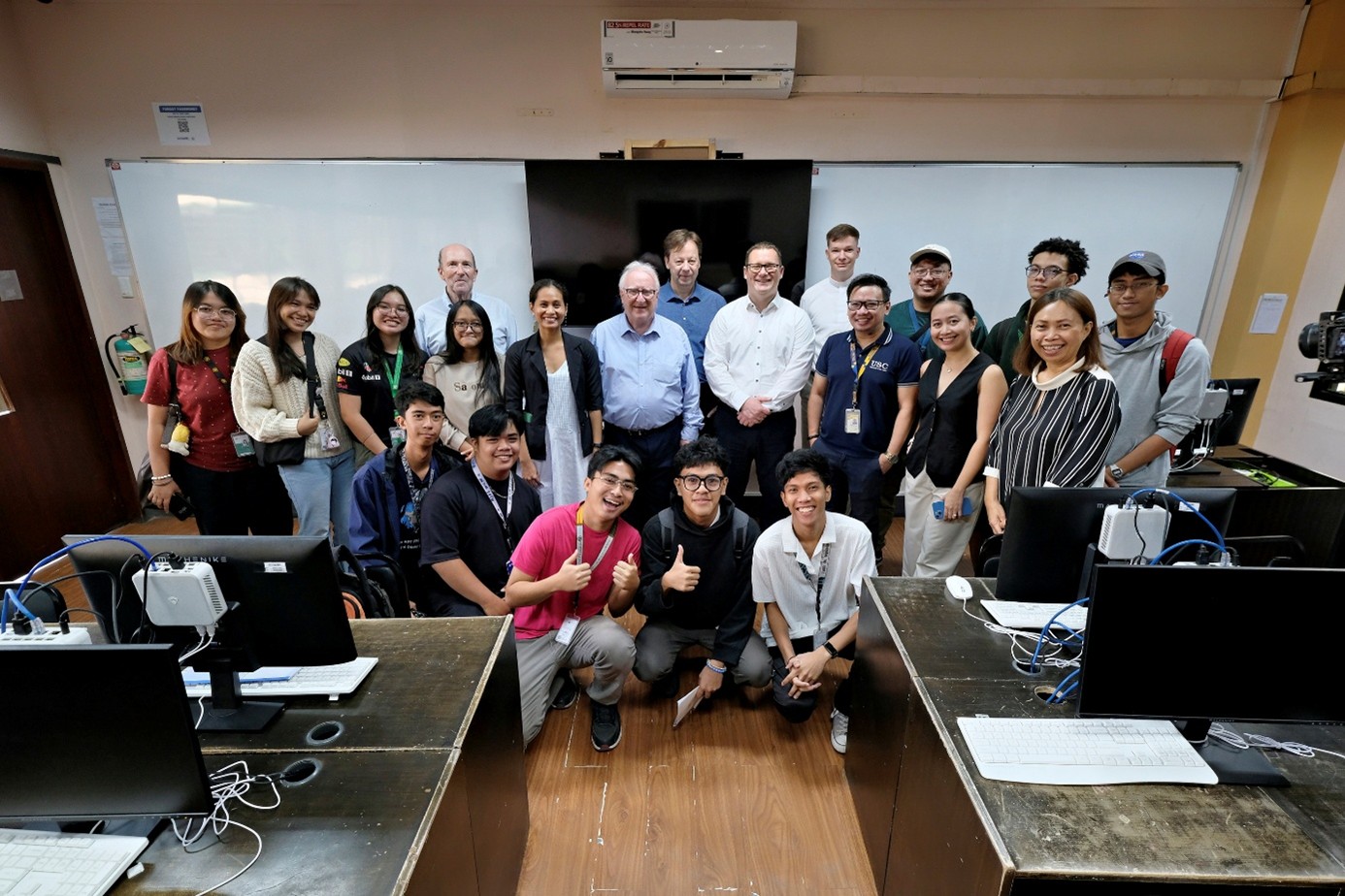 Csapatkép egy irodában, monitotokkal az asztalokon az előtérben és háttérben egy fehér tábla előtt