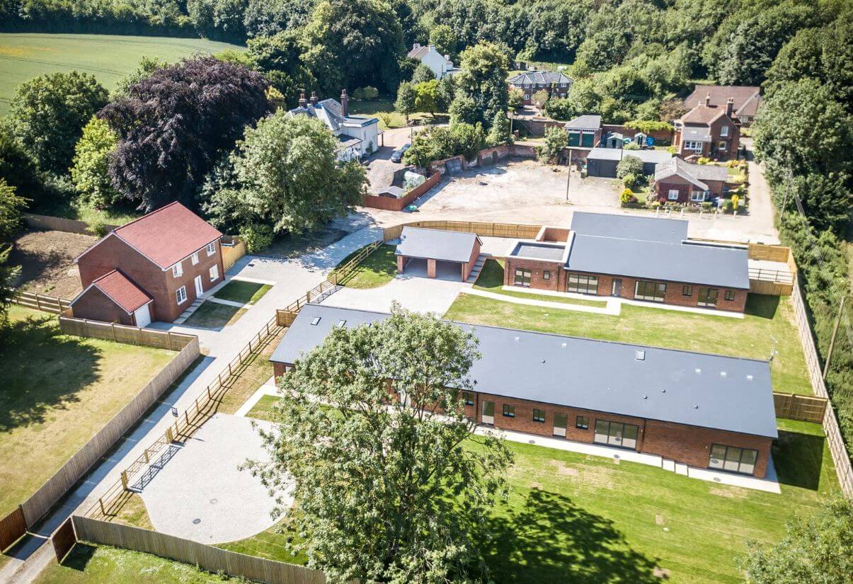 Aerial view of a residential area showing modern brick buildings with dark roofs, driveways, green lawns, and a surrounding wooden fence.