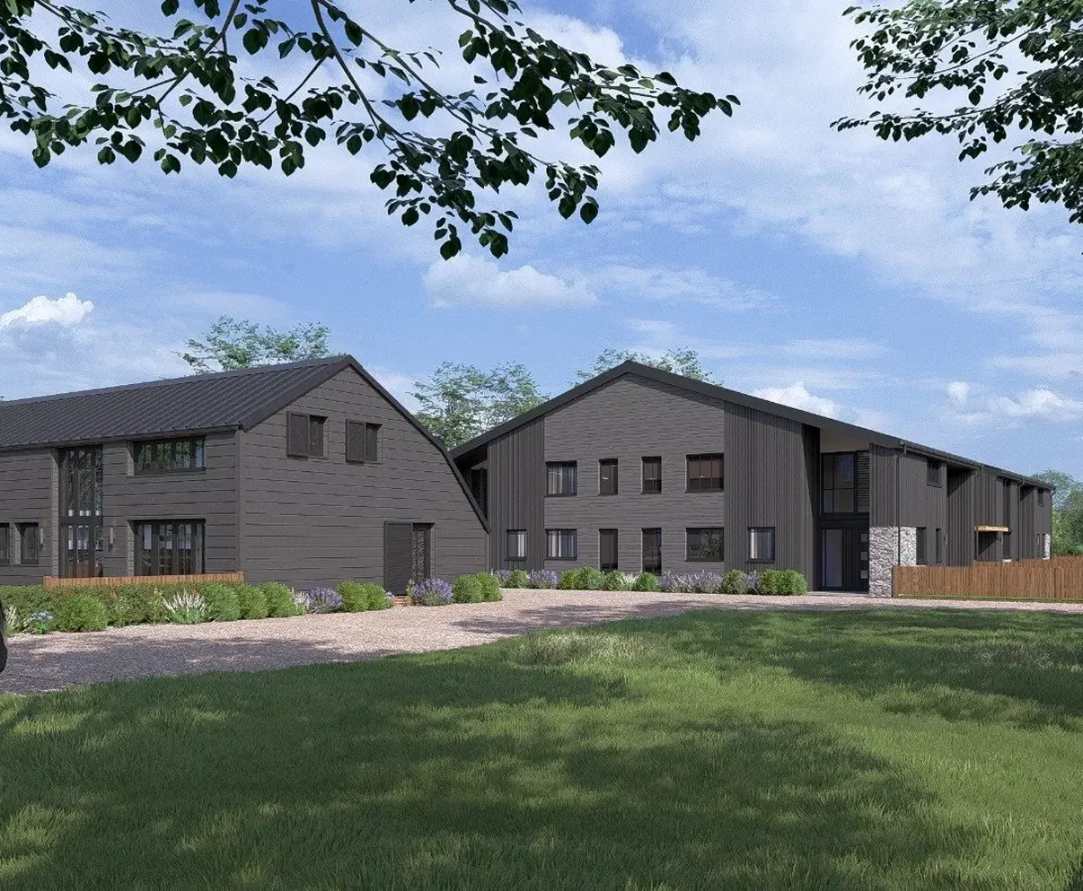 Modern dark gray two-story buildings with large windows surrounded by greenery and under a blue sky with scattered clouds.