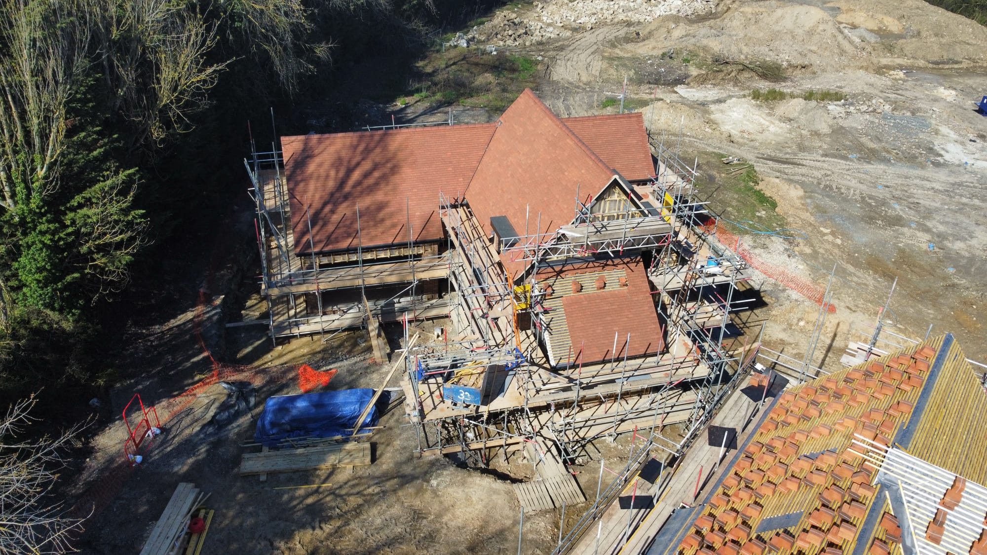 Aerial view of a house under construction surrounded by scaffolding and construction materials on a dirt site.