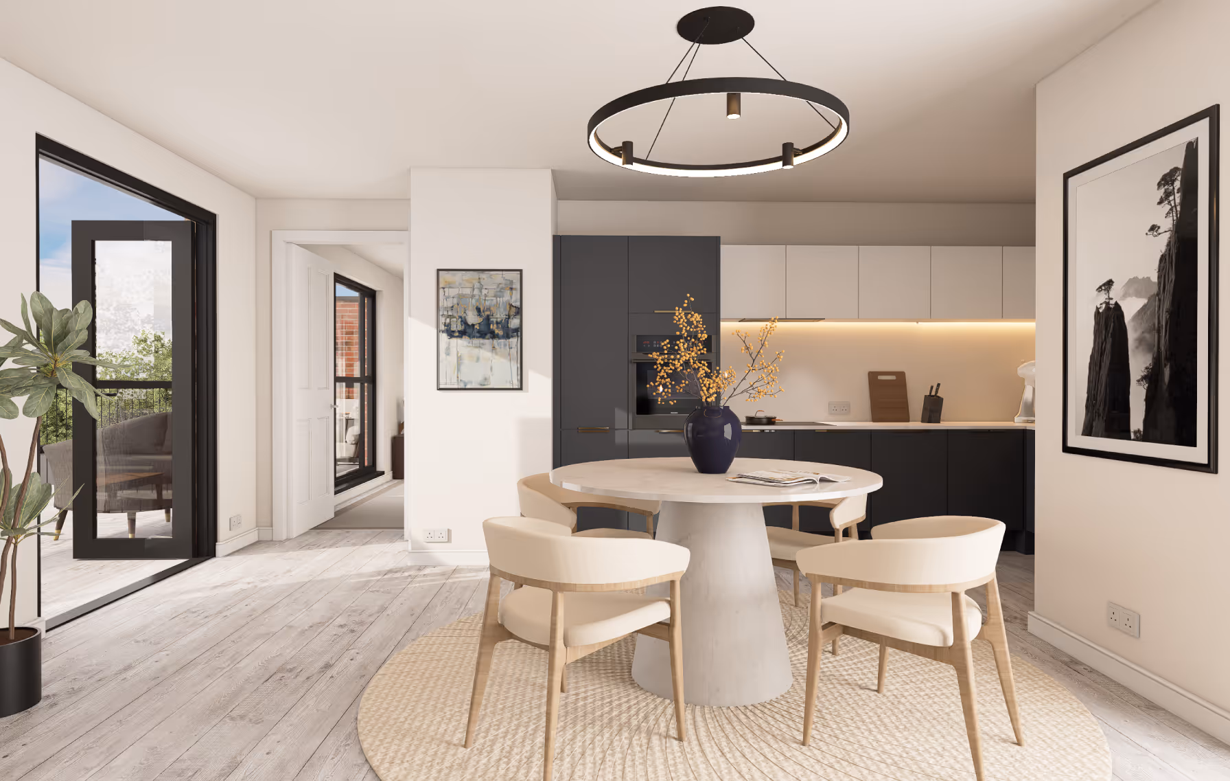Modern dining area with round table, four beige chairs, and a vase with yellow flowers, adjacent to a kitchen with dark lower cabinets and white upper cabinets.
