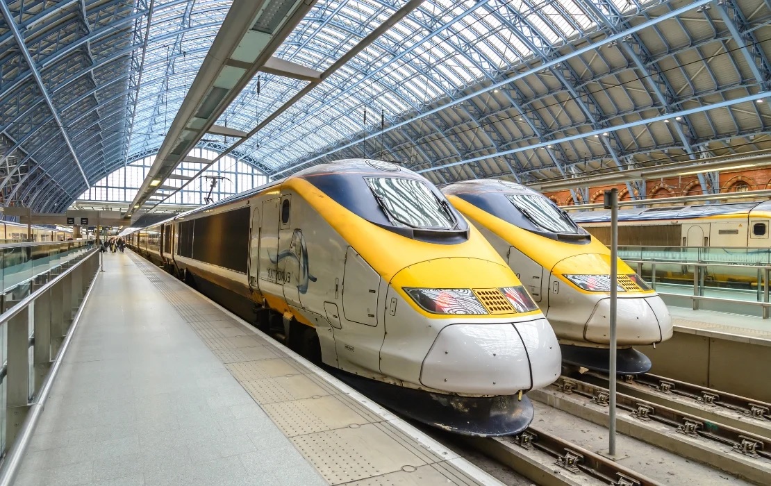 Two Eurostar high-speed trains parked side by side on tracks inside St Pancras International station with a glass roof overhead.