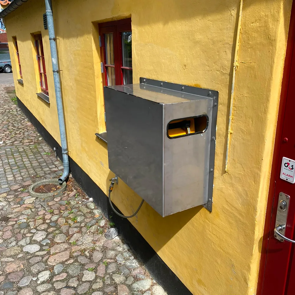 Robust, specialfremstillet kasseskjold i metal, monteret af smed på gul facade.