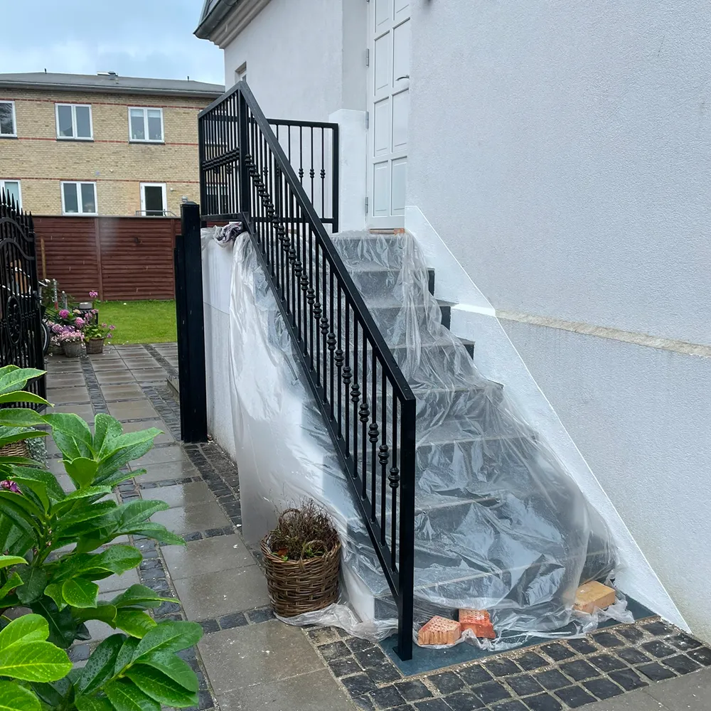 Sortlakeret stålgelænder under montage ved kældertrappe. Professionelt smedearbejde.