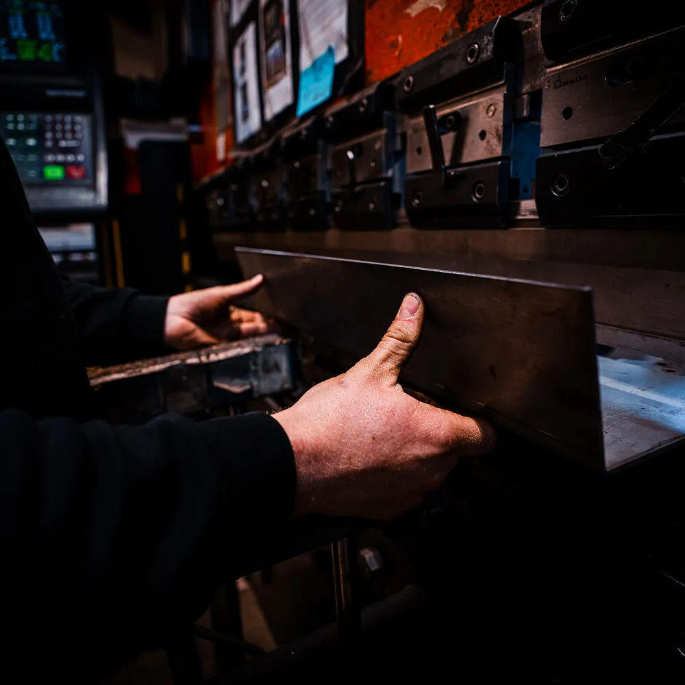 Nærbillede af hænder der betjener en maskine til metalbearbejdning.