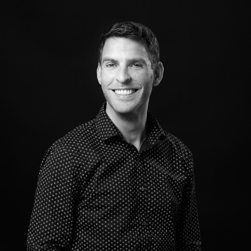 Smiling man in patterned black shirt against dark background, professional headshot