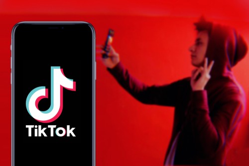 TikTok logo displayed on smartphone screen with person dancing against red background