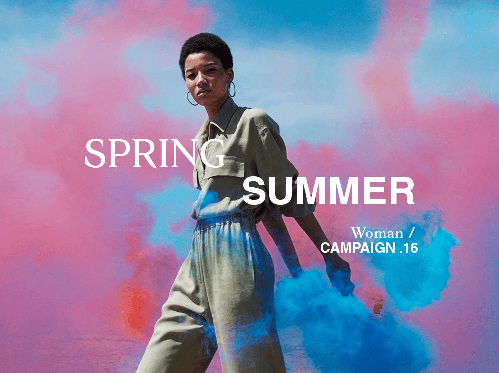 Woman in khaki jacket posing against pink and blue gradient clouds for spring summer campaign