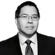 Professional headshot of a middle-aged man wearing glasses and dark suit