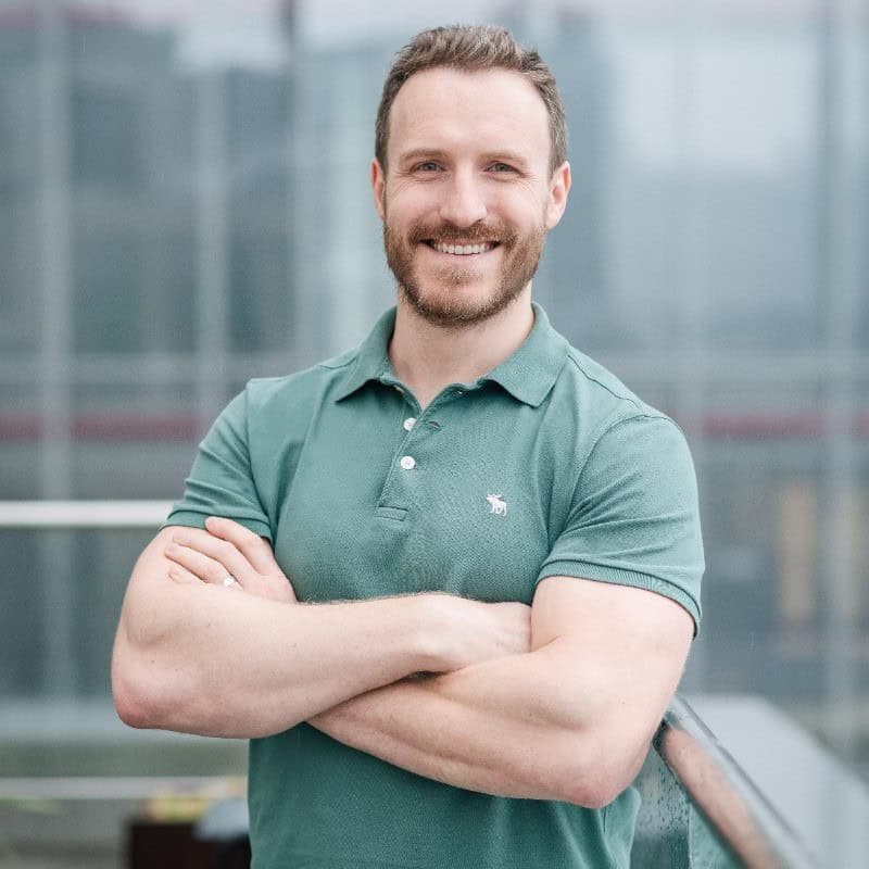 Smiling man in green polo shirt with arms crossed against urban skyline background