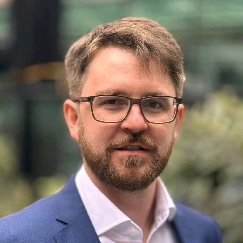Portrait of a man with glasses and beard wearing a blue blazer