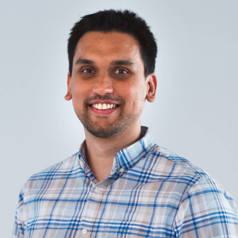 Smiling man with dark hair wearing blue and white plaid shirt