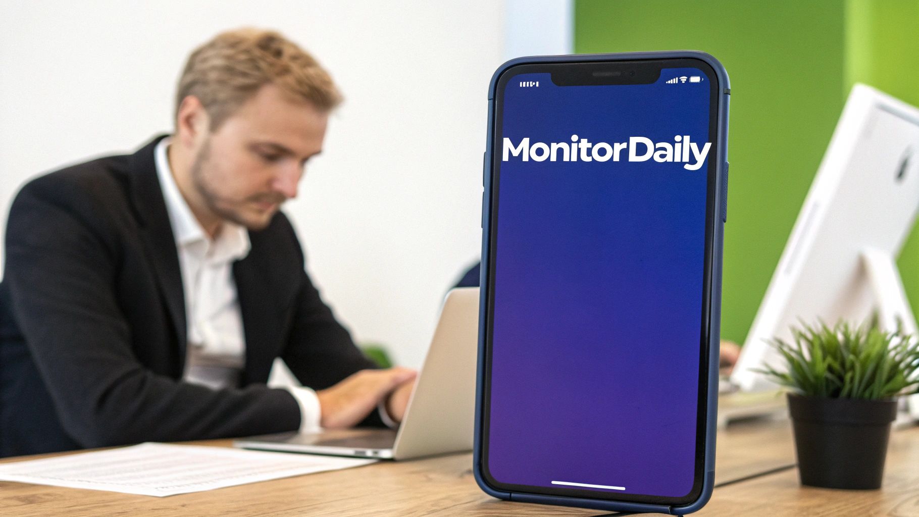 Businessman working at desk with smartphone displaying MonitorDaily app on screen
