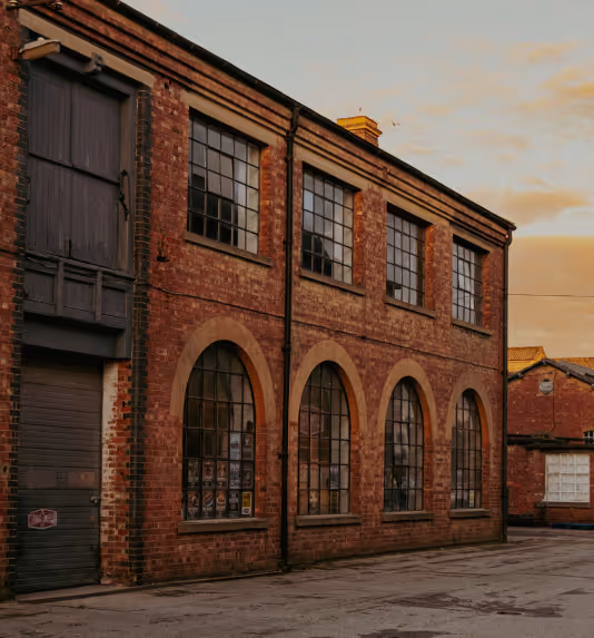 Historic two-story brick building with large arched and rectangular windows under a cloudy sky at sunset.