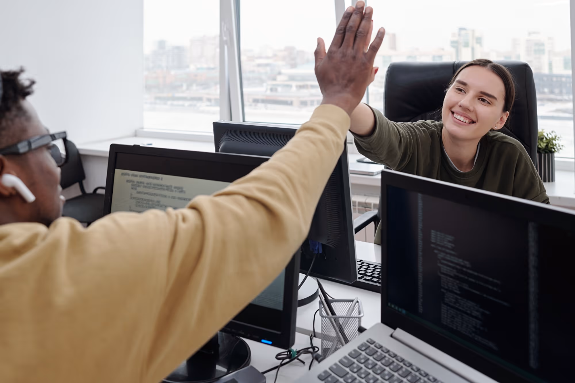 Zwei Entwickler geben sich am Schreibtisch mit mehreren Bildschirmen ein High-Five