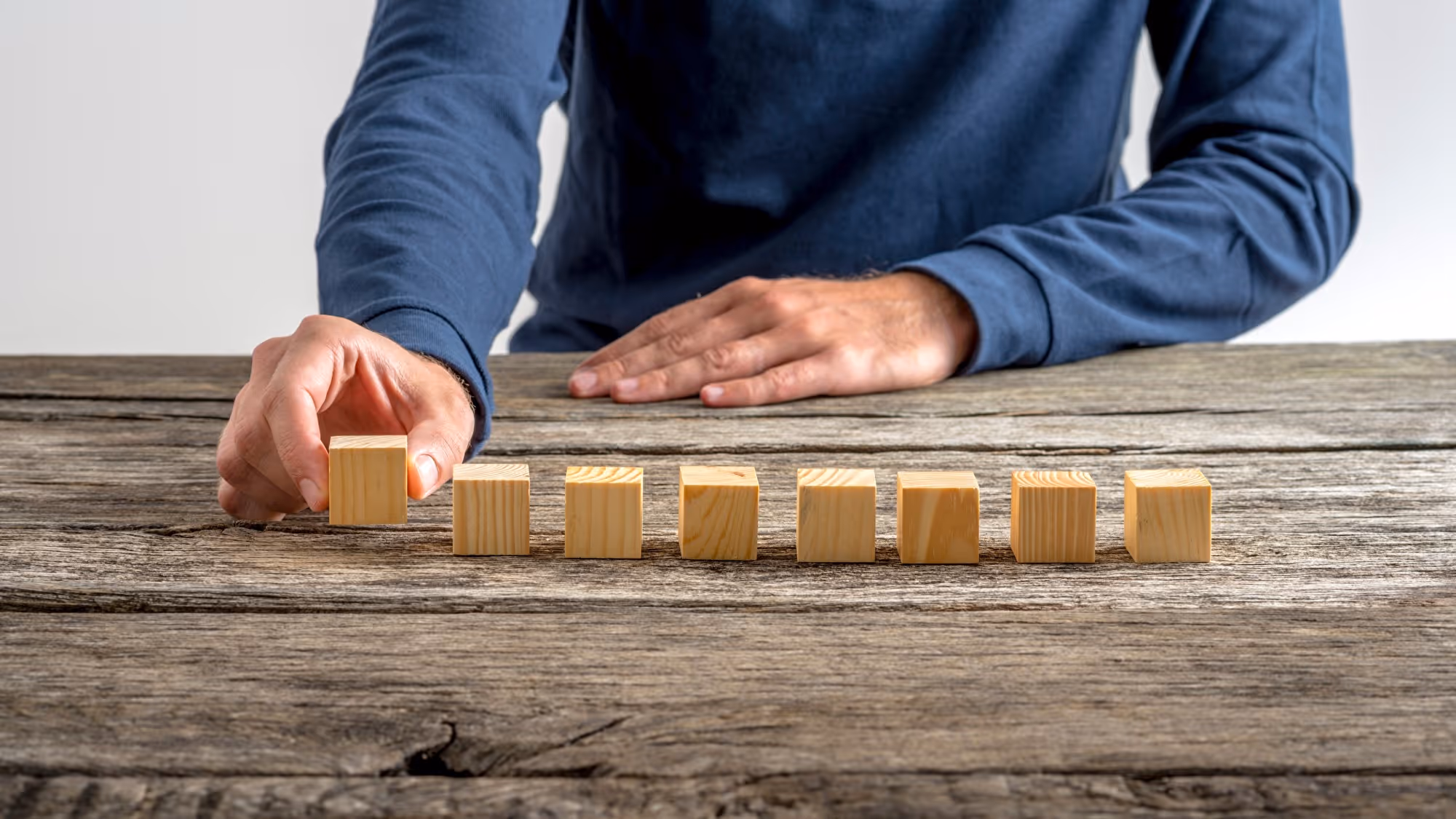 Mann legt Holzwürfel in eine Reihe auf rustikalem Holztisch als Symbol für strukturierte Planung