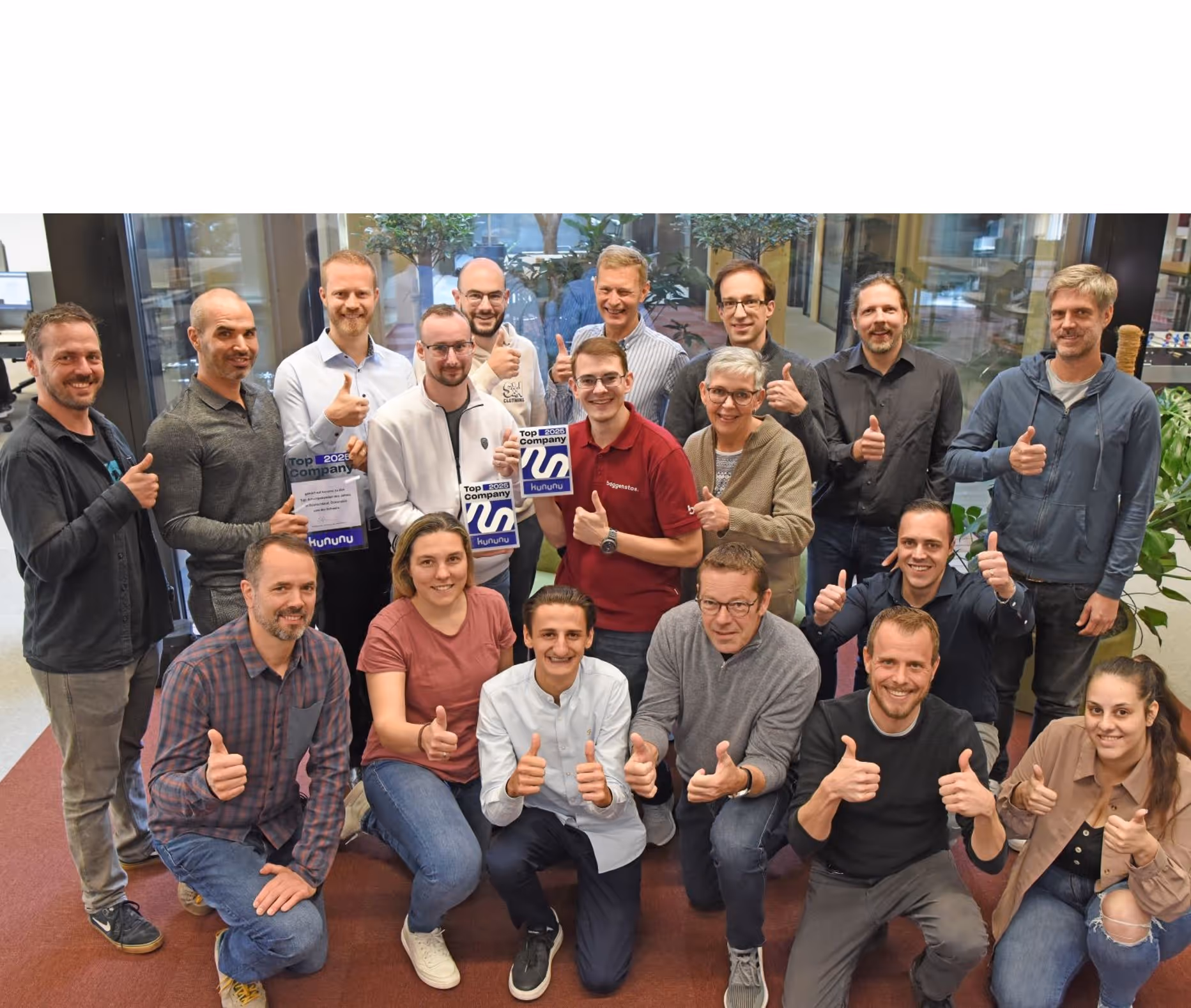 Large team group in the office smiling with thumbs up holding a kununu award.