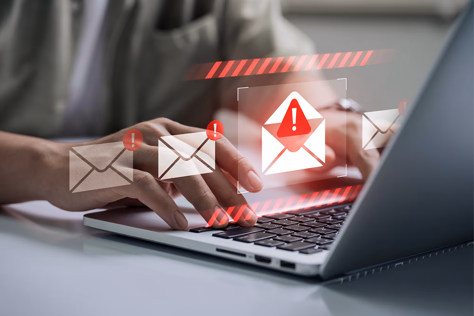 Hände tippen am Laptop, schwebende E-Mail-Symbole, eines rot mit Warnzeichen markiert.