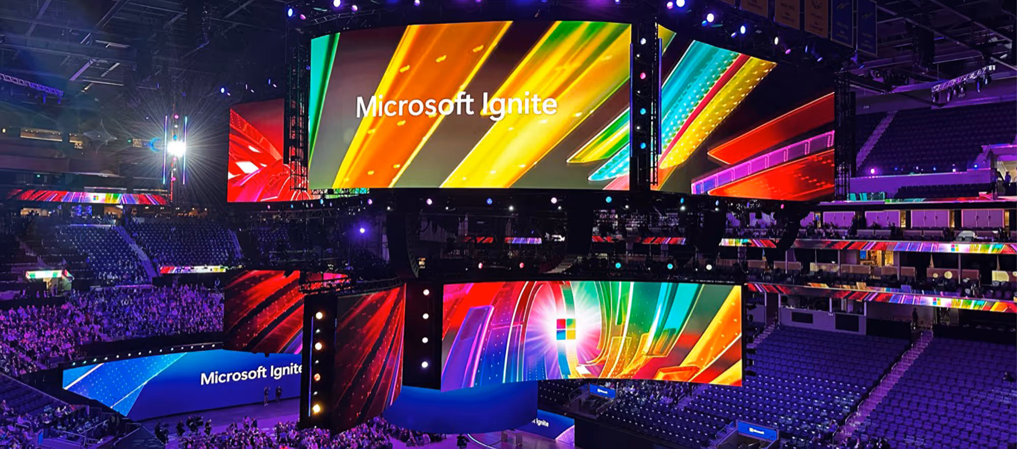 Grosse Bühnenarena mit leuchtenden Bildschirmen und dem Schriftzug «Microsoft Ignite» über leeren Zuschauerrängen.