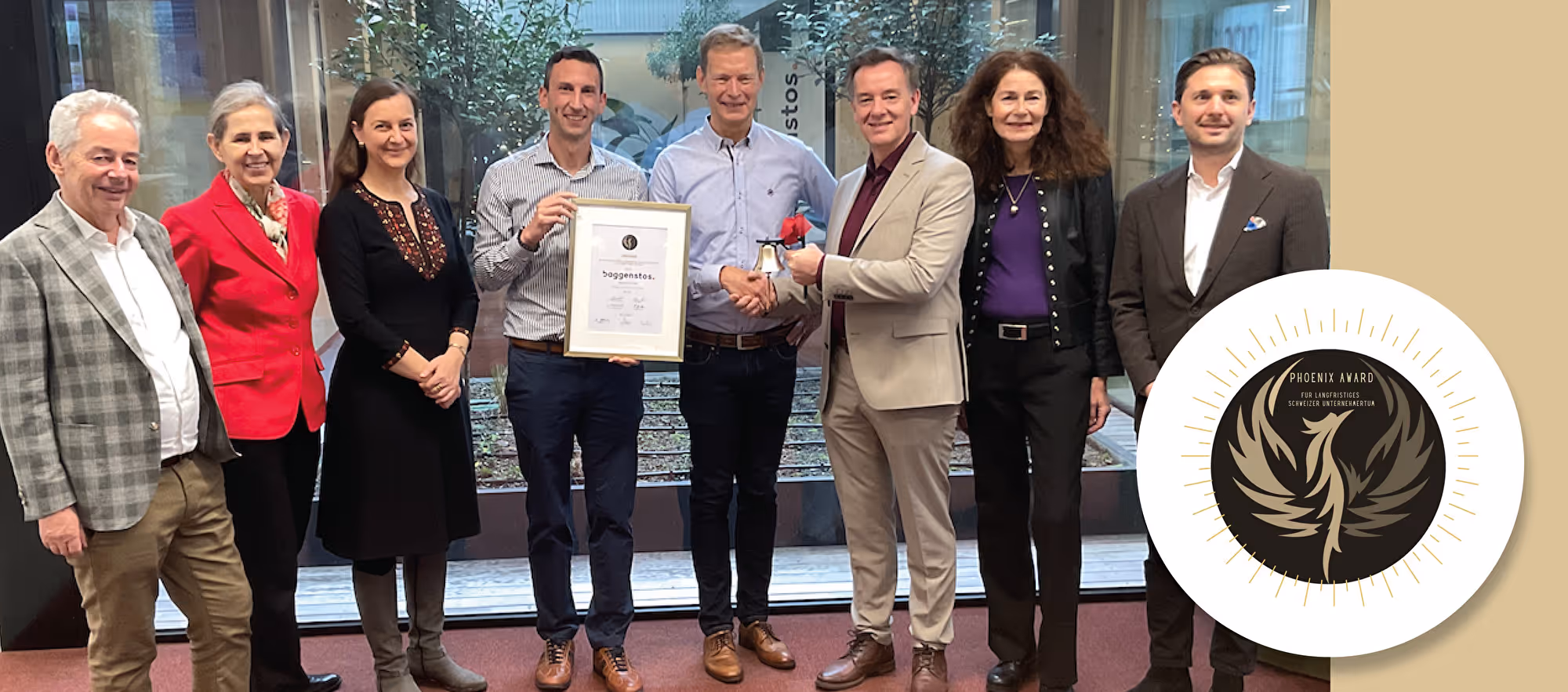 Sieben Personen stehen nebeneinander und halten gemeinsam eine gerahmte Urkunde, daneben das goldene Phoenix-Award-Emblem.