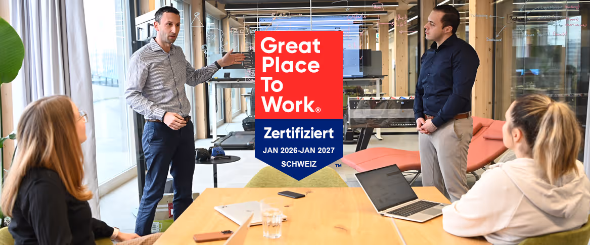 Vier Personen in einer Besprechung im modernen Büro, Great-Place-to-Work-Zertifikat im Bild eingeblendet