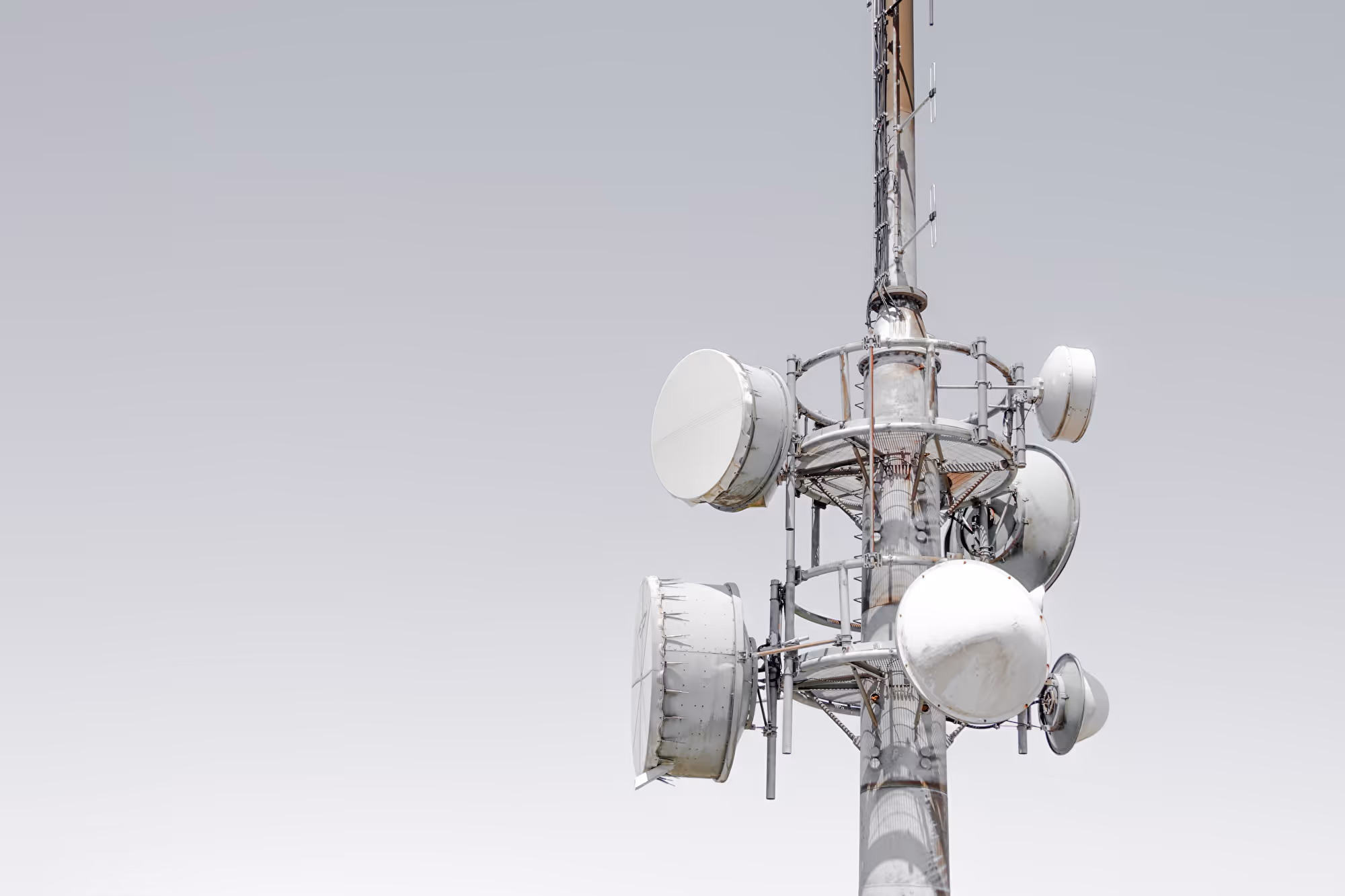 Funkmast mit mehreren runden Richtfunkantennen vor hellgrauem Himmel.