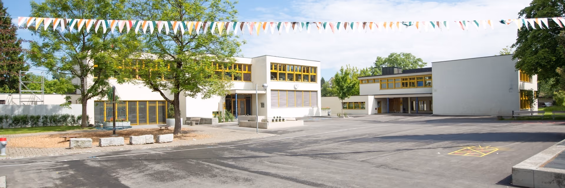 School building with yellow windows and an empty schoolyard, colourful bunting strung above.