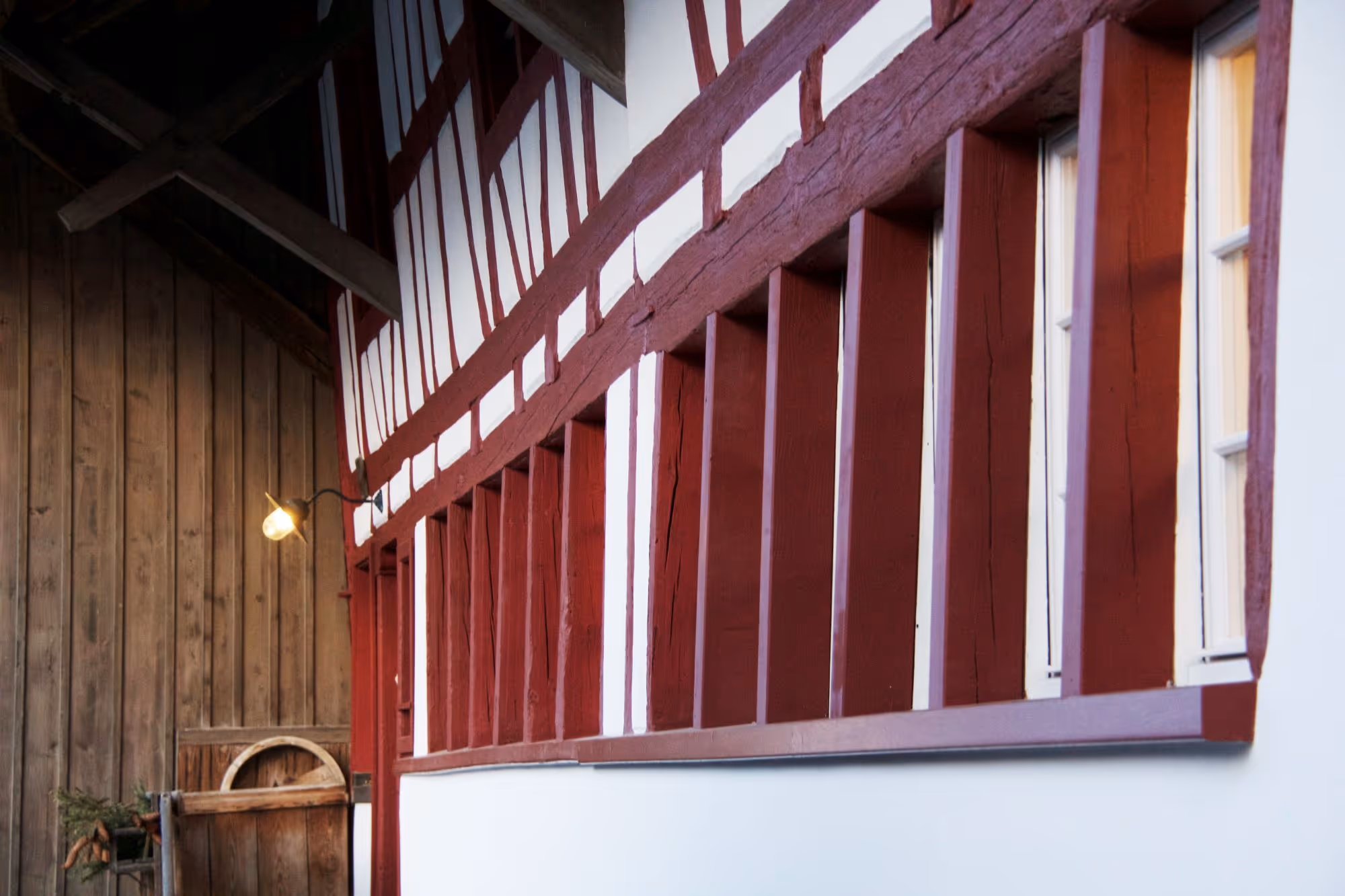Rot gestrichene Riegelfassade eines Fachwerkhauses mit Holzwand und Lampe im Innenhof.