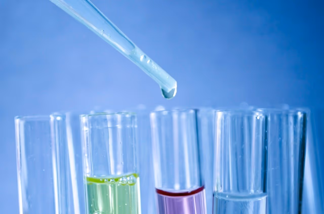 Symbolbild: Pipette tropft Flüssigkeit in Reagenzgläser mit farbigen Proben