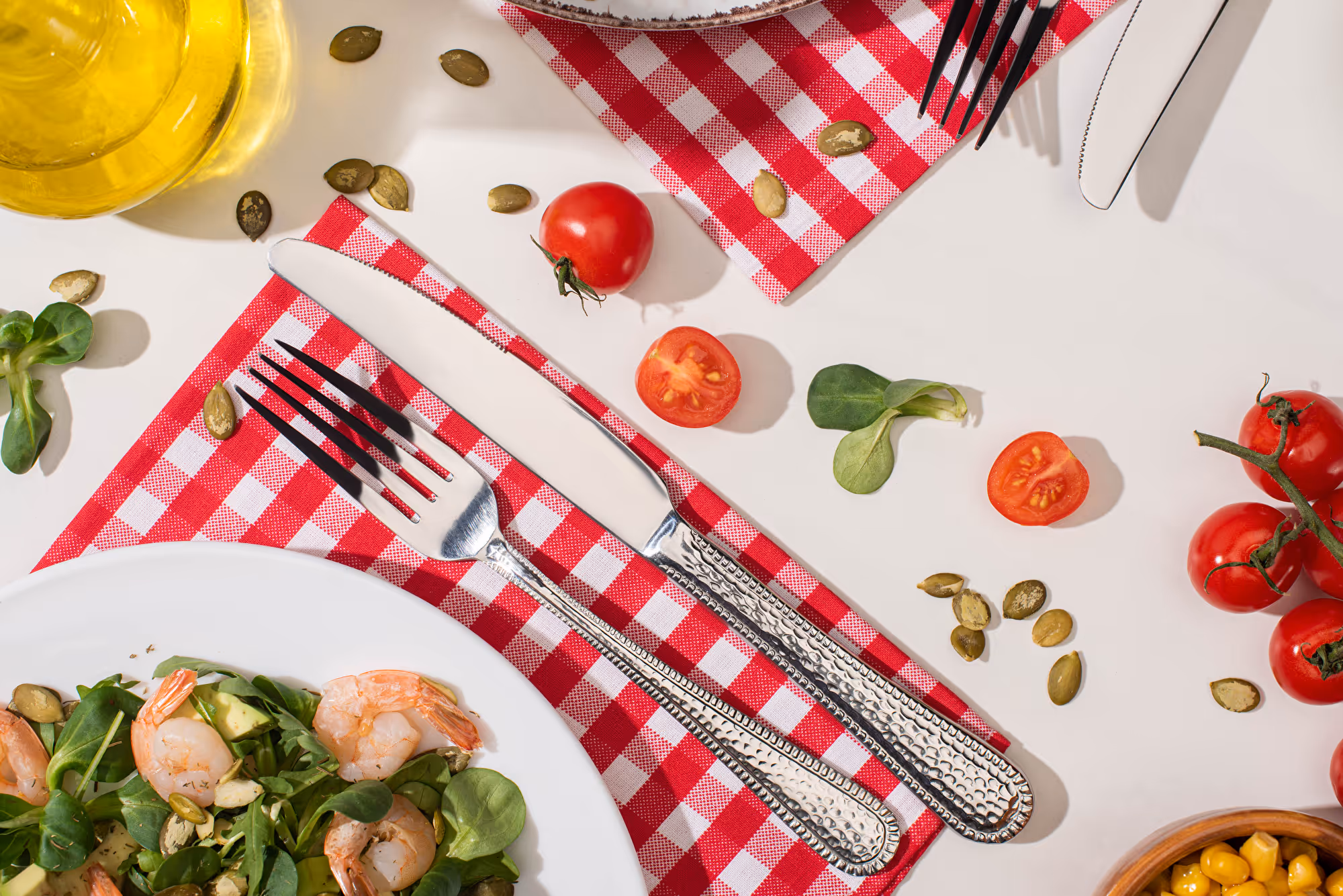 Frischer Salat mit Crevetten, Gabel und Messer auf rot-weiss kariertem Tuch mit Tomaten
