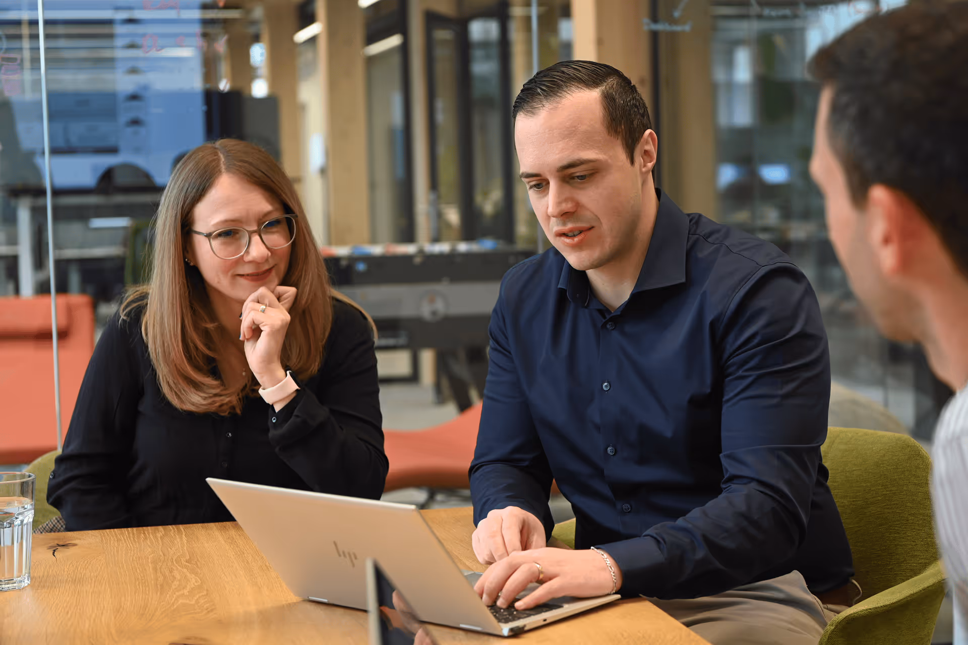 Frau und Mann blicken gemeinsam auf einen Laptop in einem modernen Büro