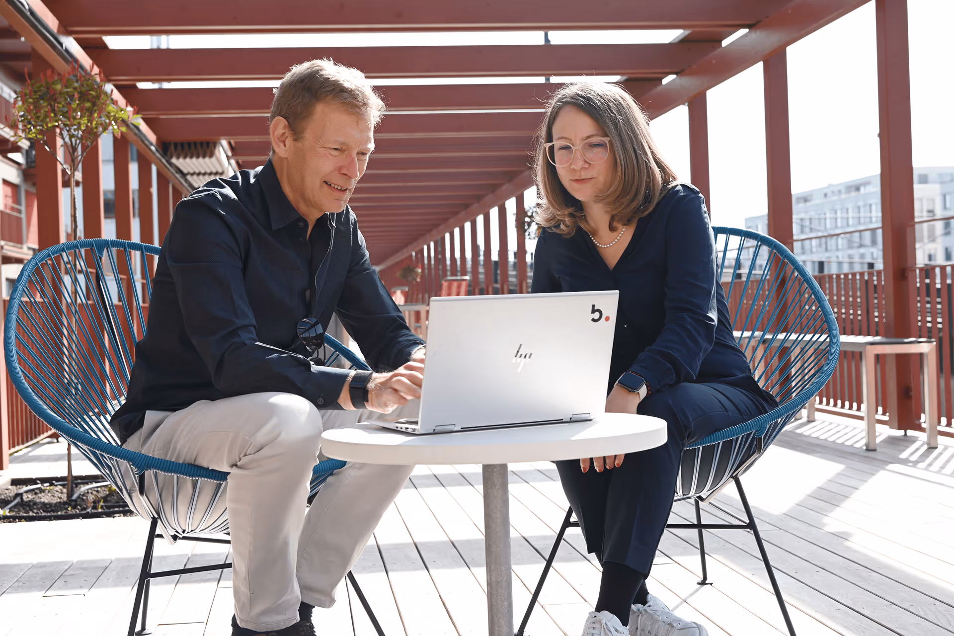 Mann und Frau arbeiten gemeinsam am Laptop auf einer sonnigen Aussenterrasse